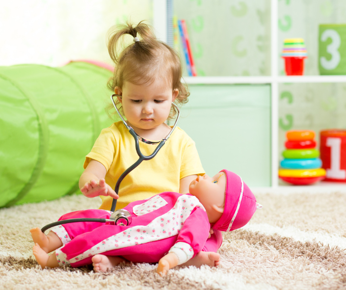 The child is playing with stethoscope, holding a doll on her knees The child is playing with stethoscope, holding a doll on her knees